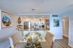 Een moderne keuken met roestvrijstalen apparatuur, een eethoek met een glazen tafel en comfortabele stoelen, en kunstwerken aan de wanden.