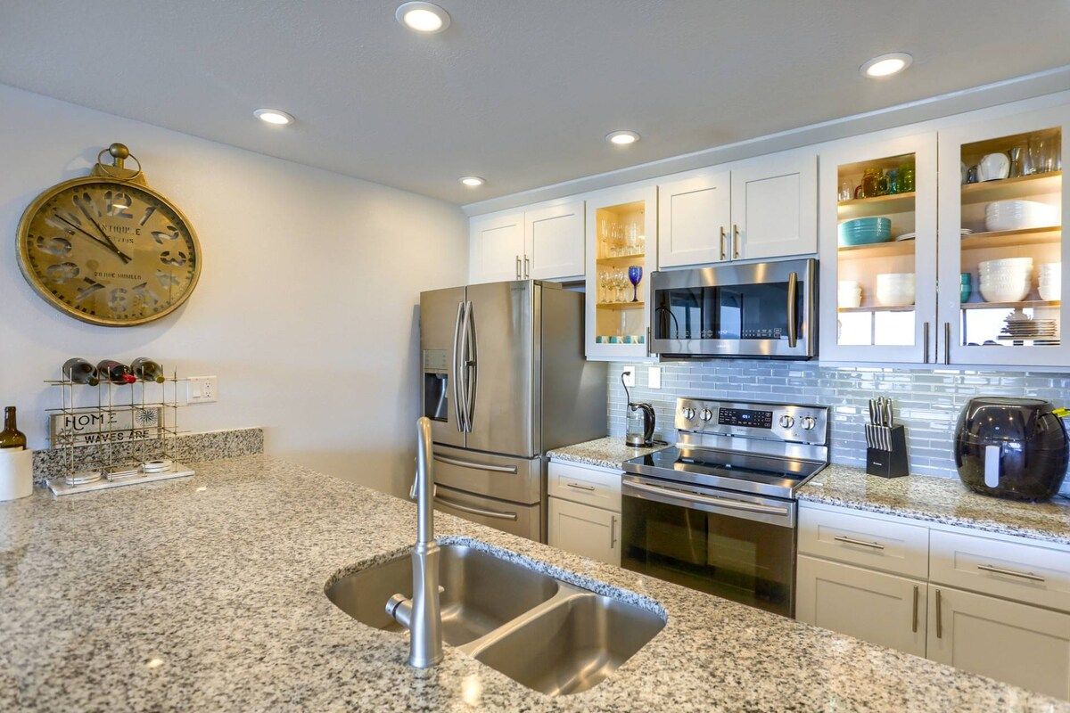 A modern kitchen with granite countertops, stainless steel appliances, and a clock on the wall.