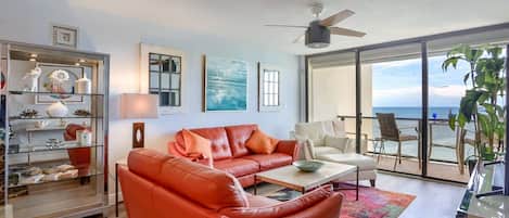 Una sala de estar moderna con un sofá de cuero rojo, un sillón blanco y una mesa de centro de vidrio. Hay un ventanal con vistas al océano.