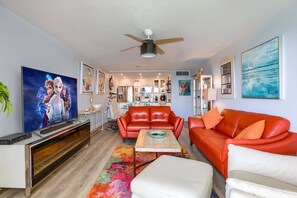 A living room with a red sofa, a white armchair, a coffee table, and a TV displaying animated characters.