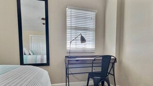 A bedroom with a bed, a desk with a chair, a window with blinds, and a mirror. - Ocean View Overlooking Marina Ocean Pointe 5305 (Tavernier)