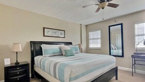 A bedroom with a bed, a nightstand, a lamp, a ceiling fan, a window with blinds, and a mirror. - Ocean View Overlooking Marina Ocean Pointe 5305 (Tavernier)