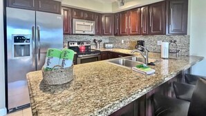 A modern kitchen with dark wood cabinets, stainless steel appliances, granite countertops, and a built-in oven. - Ocean View Overlooking Marina Ocean Pointe 5305 (Tavernier)