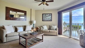 A spacious living room with a ceiling fan, two sofas, a coffee table, and a large window offering a view of the ocean. - Ocean View Overlooking Marina Ocean Pointe 5305 (Tavernier)