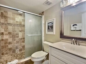 A bathroom with a glass-enclosed shower, a toilet, a sink, and a mirror. - Marina & Ocean View 2BR | Ocean Pointe 5305 (Tavernier)
