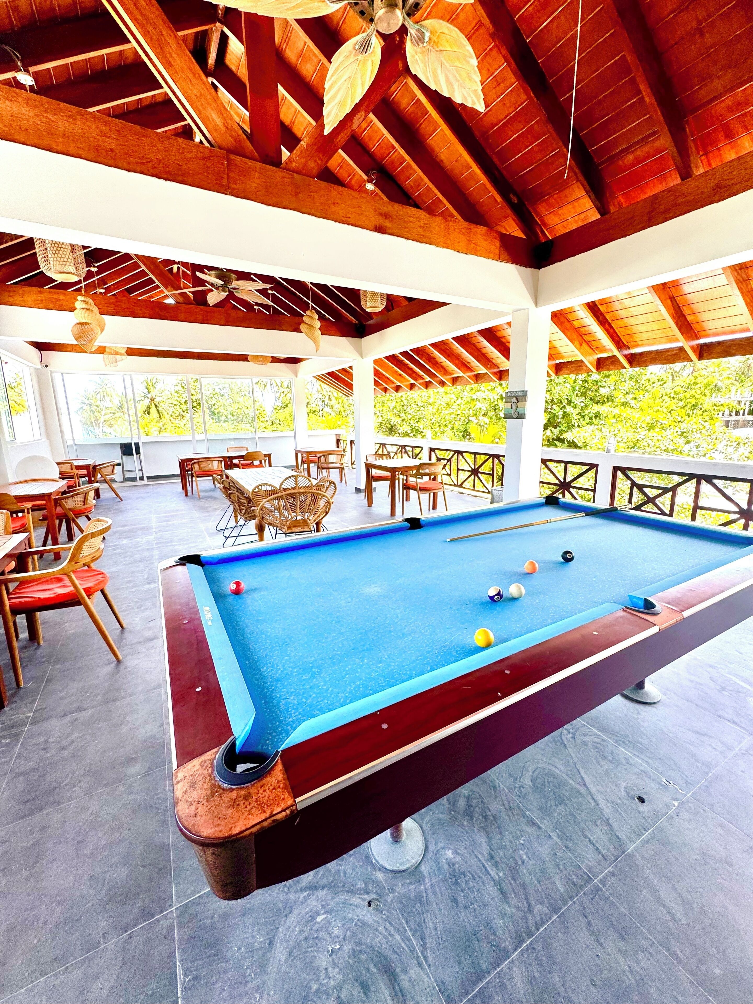 A pool table in a covered outdoor area with wooden beams and hanging lights.