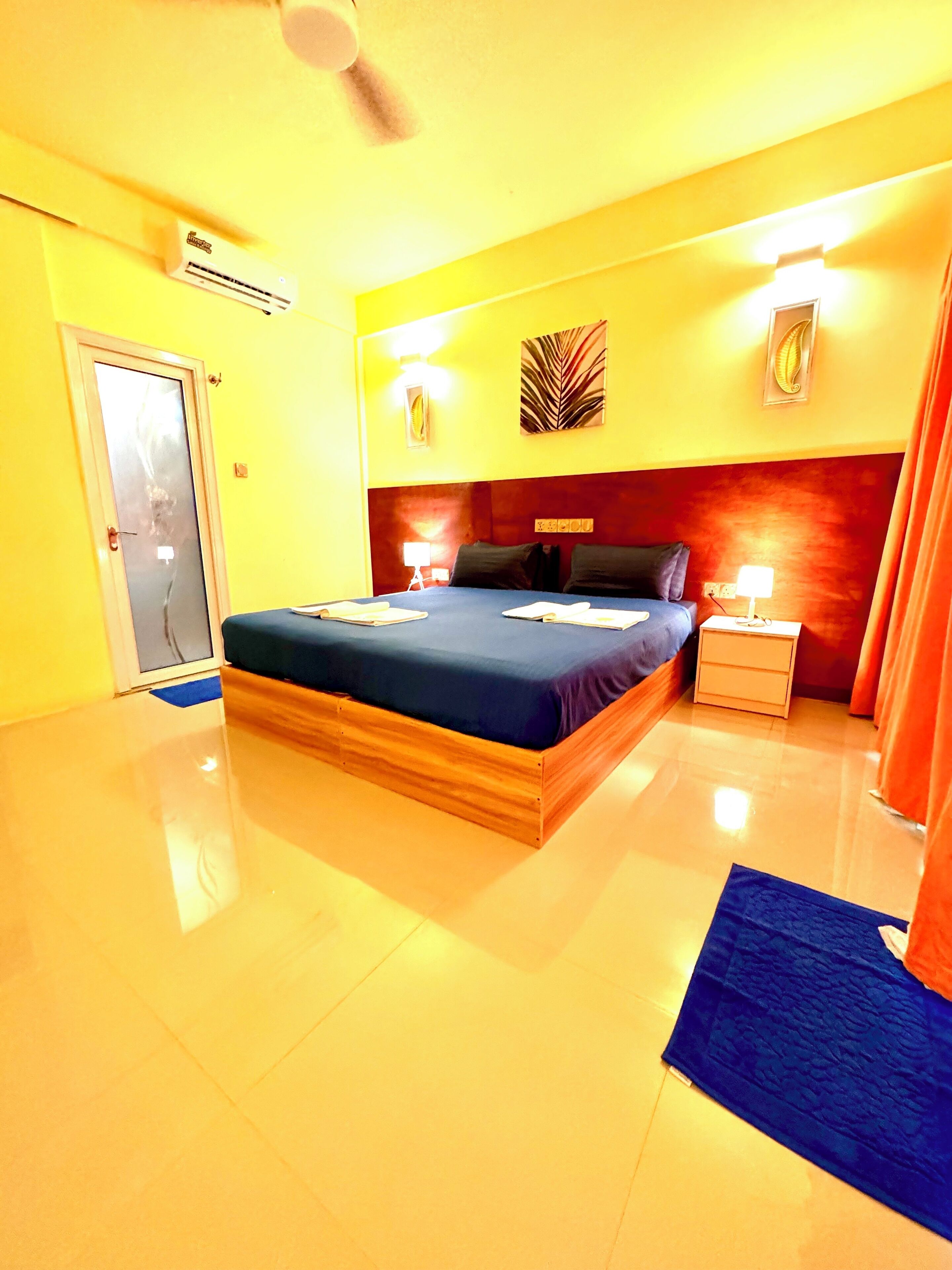 Quarto de hotel com uma cama grande, mesa de cabeceira, ventoinha no teto e uma porta.