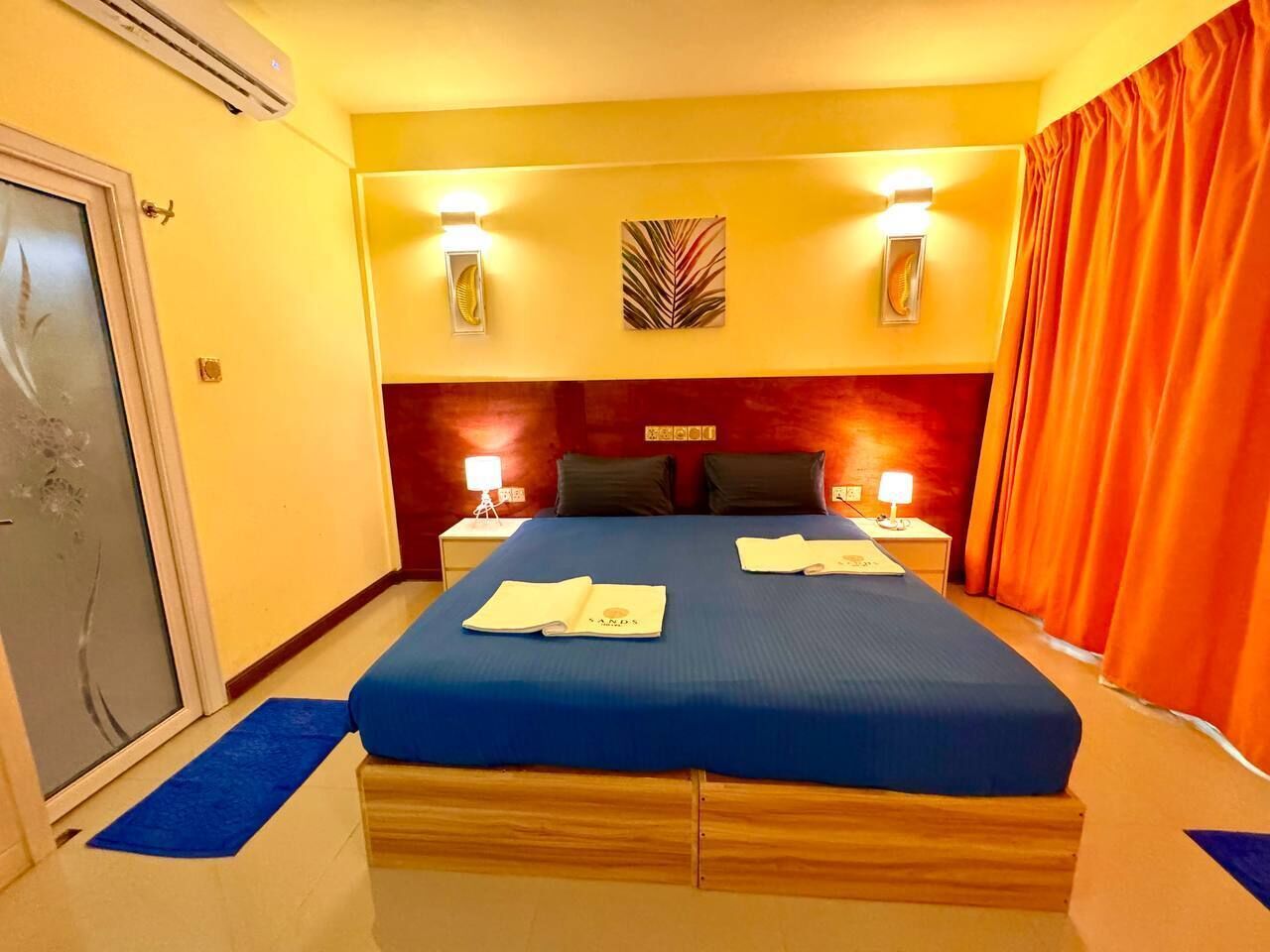 Quarto de hotel com uma cama grande, duas mesas de cabeceira com luminárias, uma obra de arte na parede e uma porta deslizante.