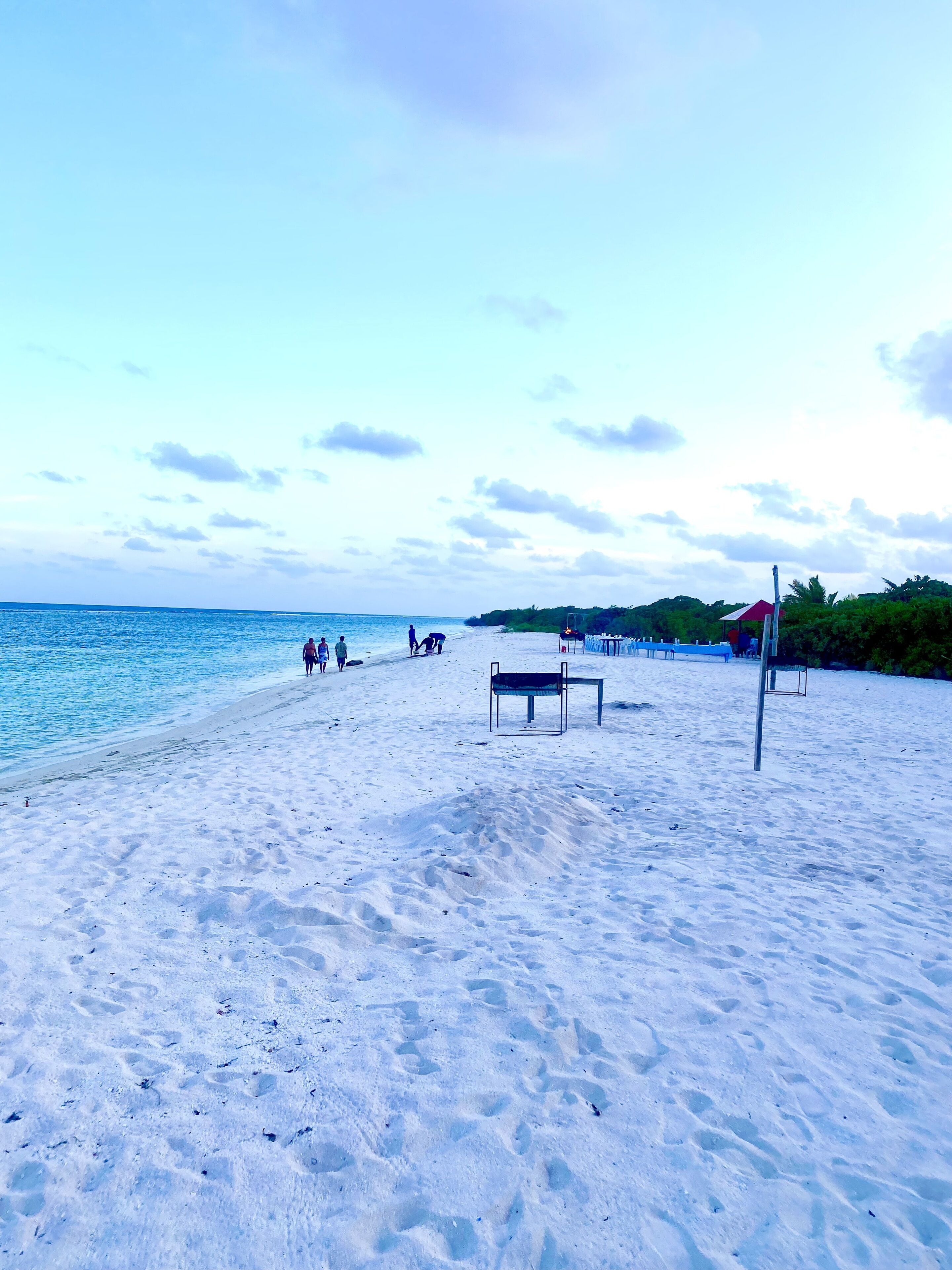 Une plage où quelques personnes se promènent, une table et une structure surmontée d’un toit rouge.