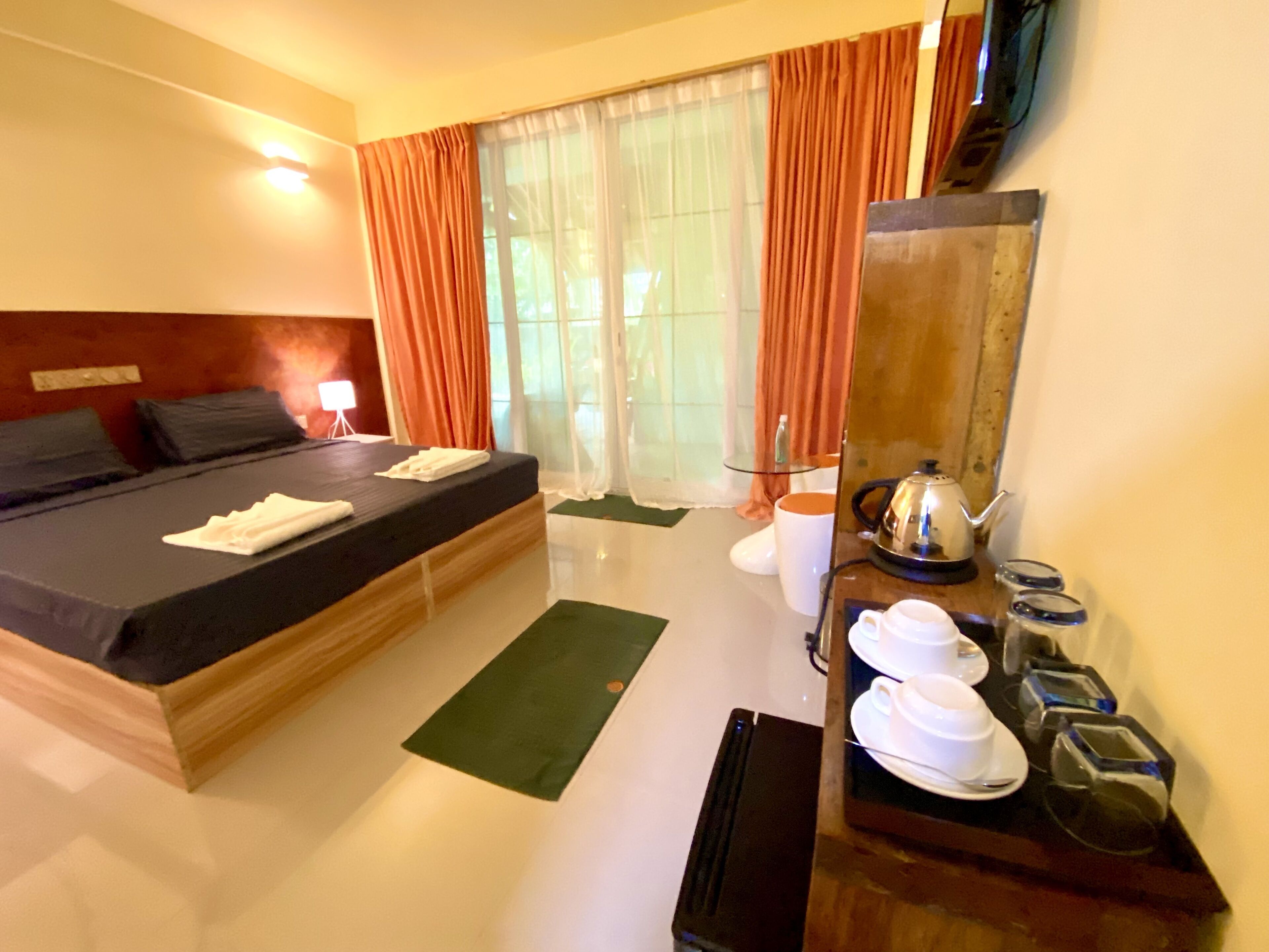 Una habitación de hotel con una cama, un escritorio con una tetera, tazas y un espejo.