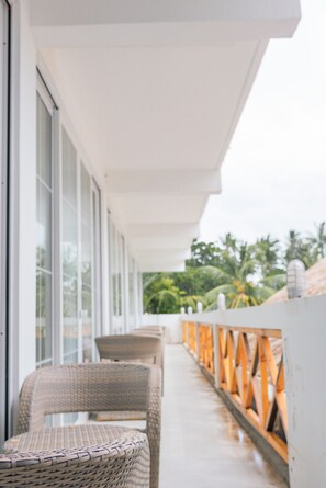 A balcony with wicker furniture and a view of palm trees. - Sands Grand Hotel (Dhigurah)