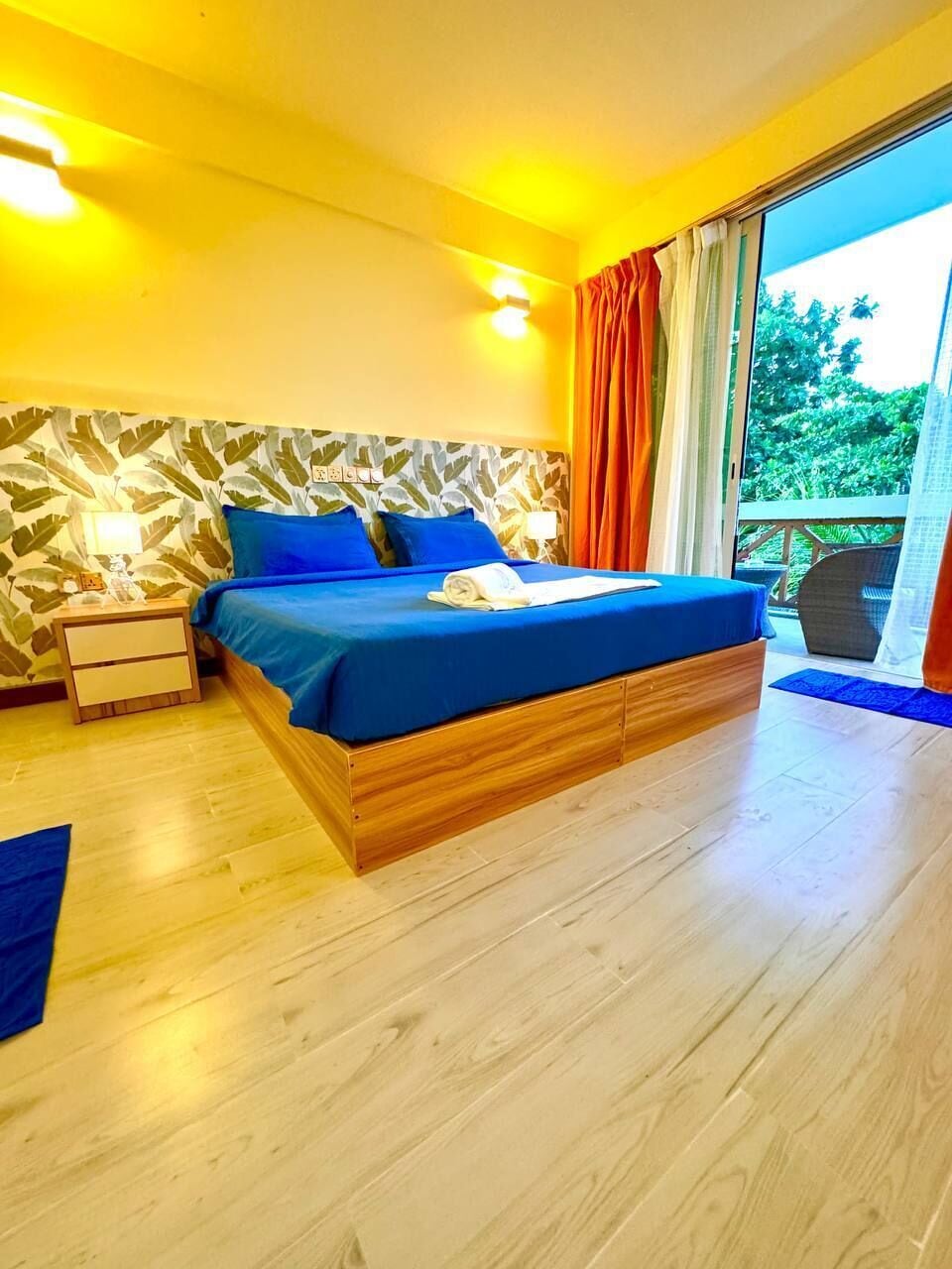 Quarto com cama, mesas de cabeceira, janela com cortinas e vista para o verde lá fora.