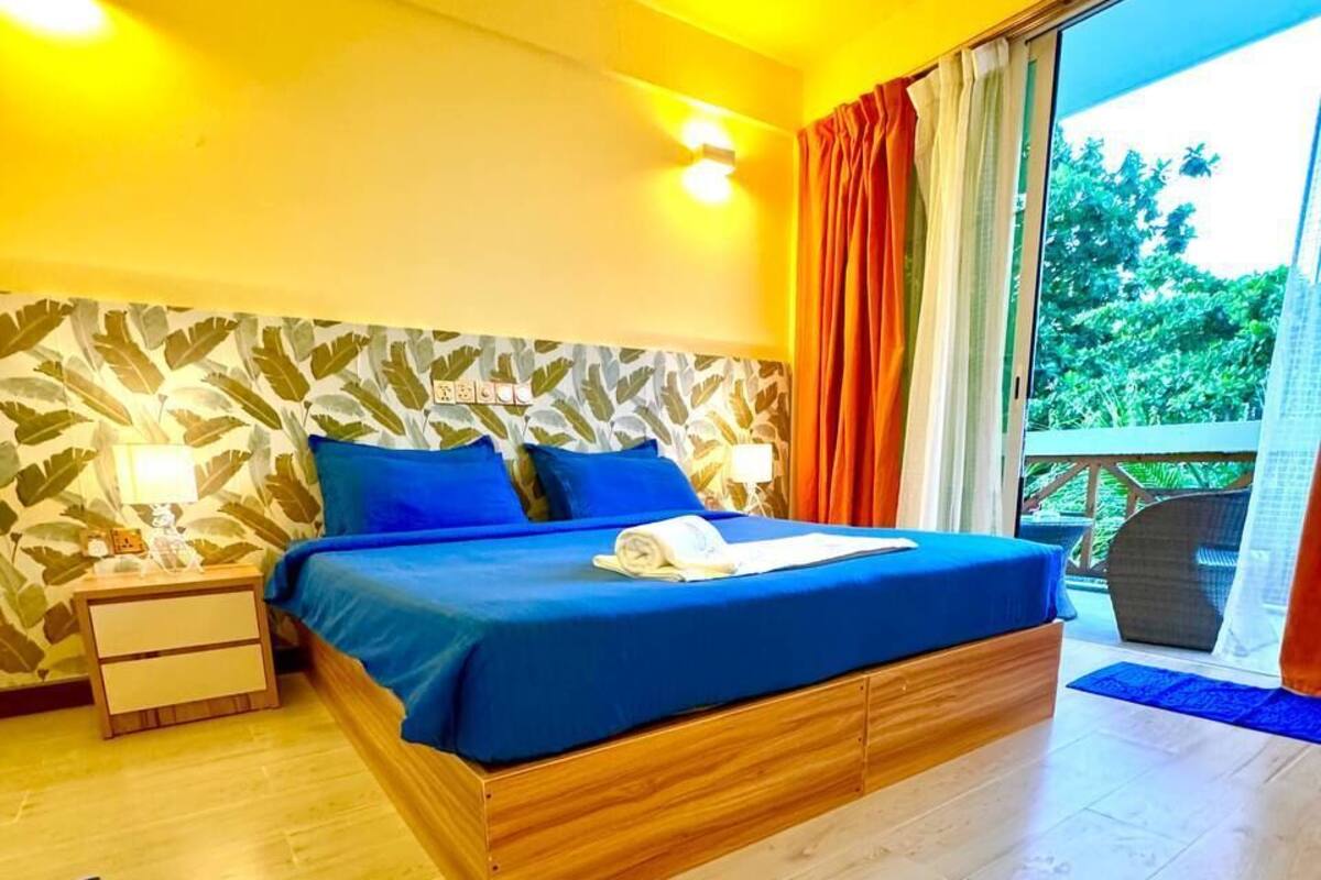 A bedroom with a bed, nightstands, a window with curtains, and a view of greenery outside.