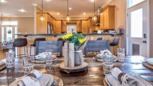 Un coin repas avec une table en bois dressée pour quatre personnes, agrémentée de verres, d’assiettes et d’un centre de table composé de fleurs.