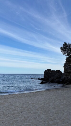 A beach with clear skies, calm water, and rocky cliffs.