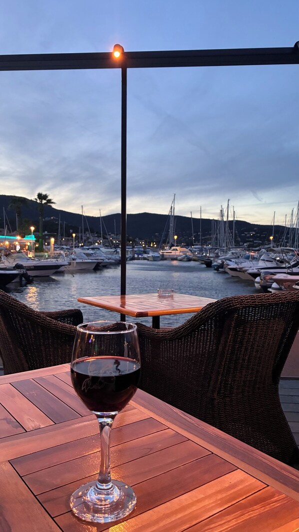 A glass of red wine on a wooden table with a view of a marina at dusk.