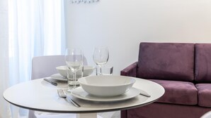 A dining table with white plates, bowls, and cutlery, set against a purple sofa. - Italianway - The B Village Business - 10 (Milan)