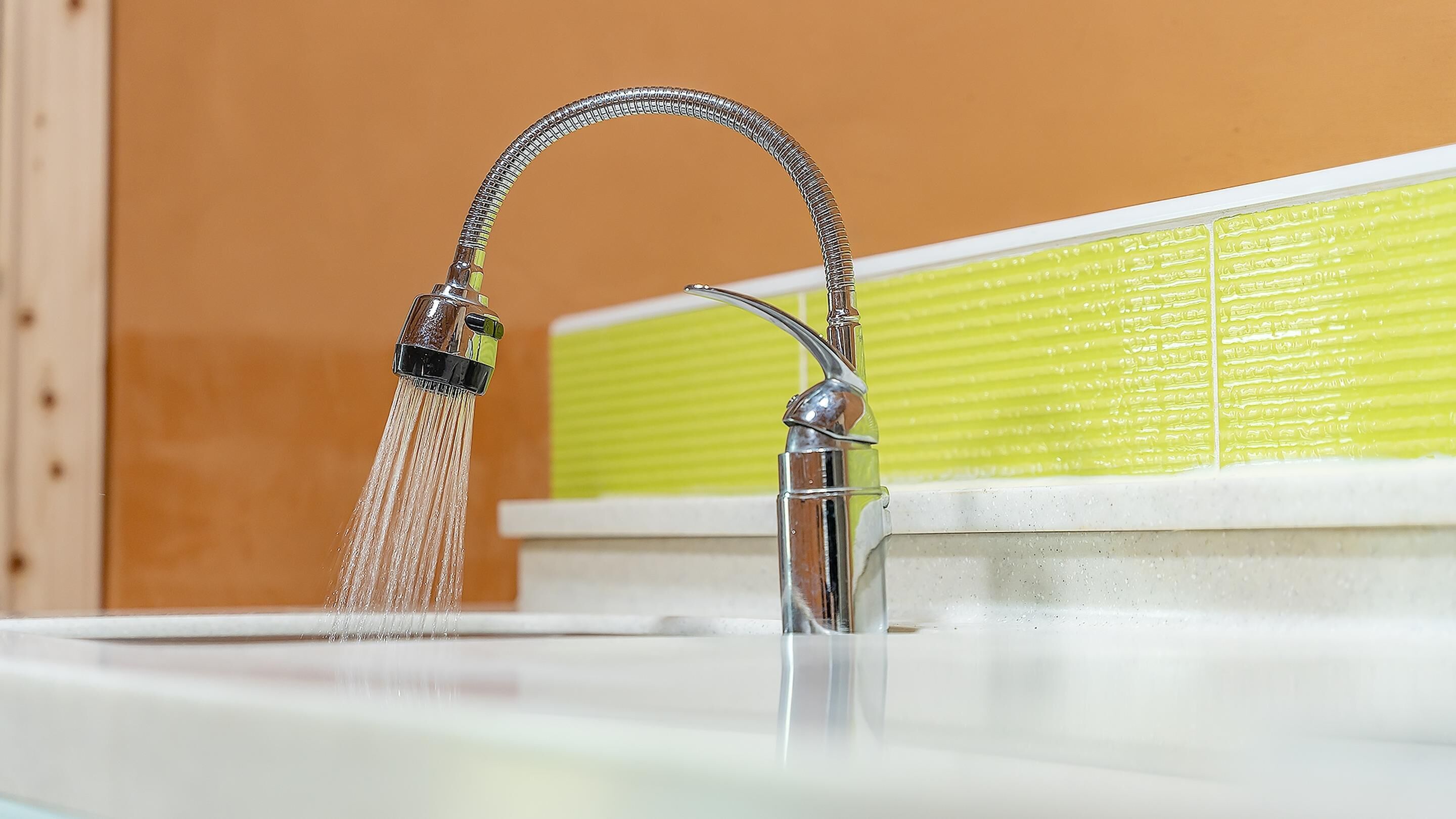 A bathroom with a chrome faucet and a green tiled wall.