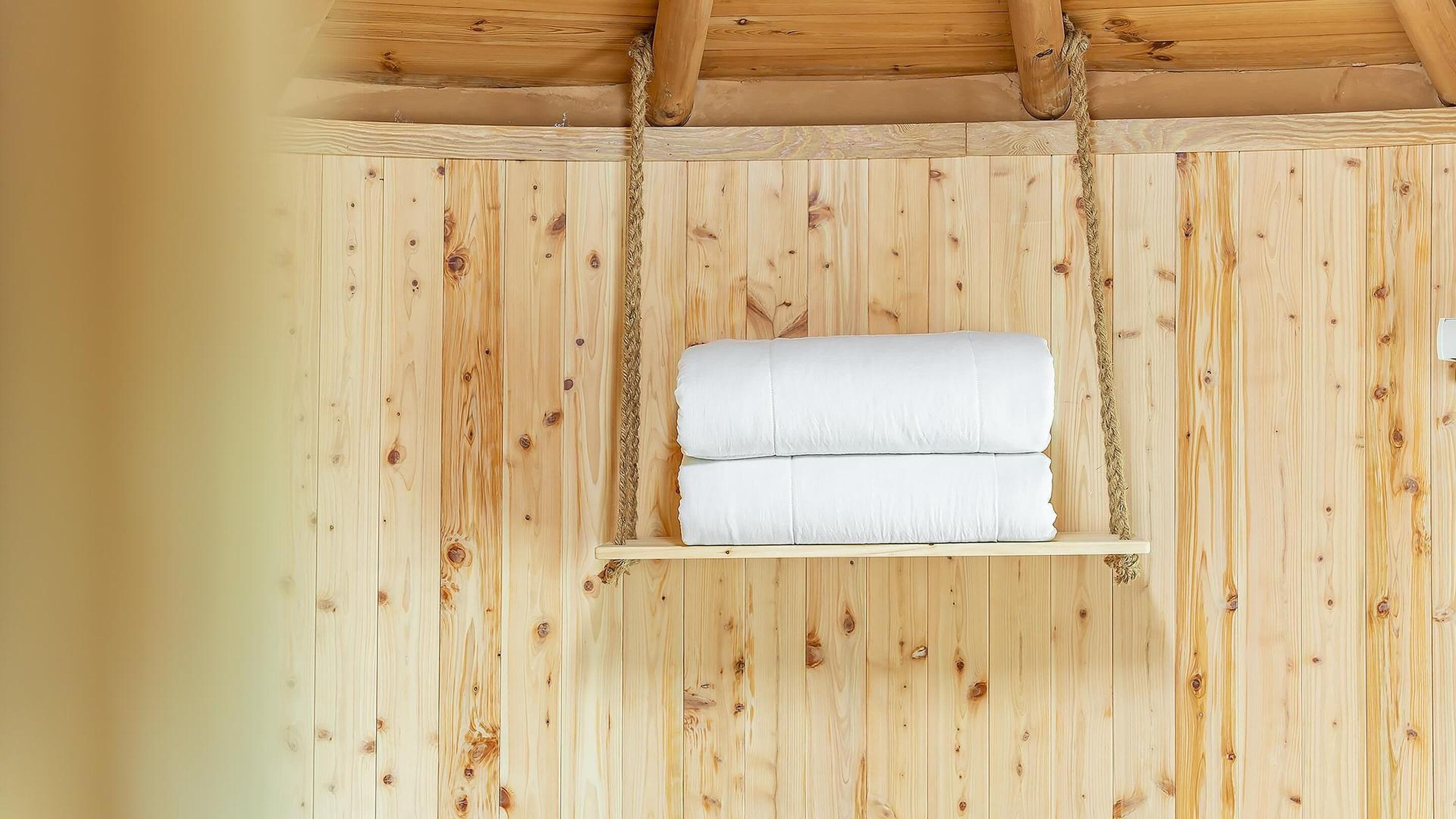 A wooden wall with a shelf holding two rolled white towels.