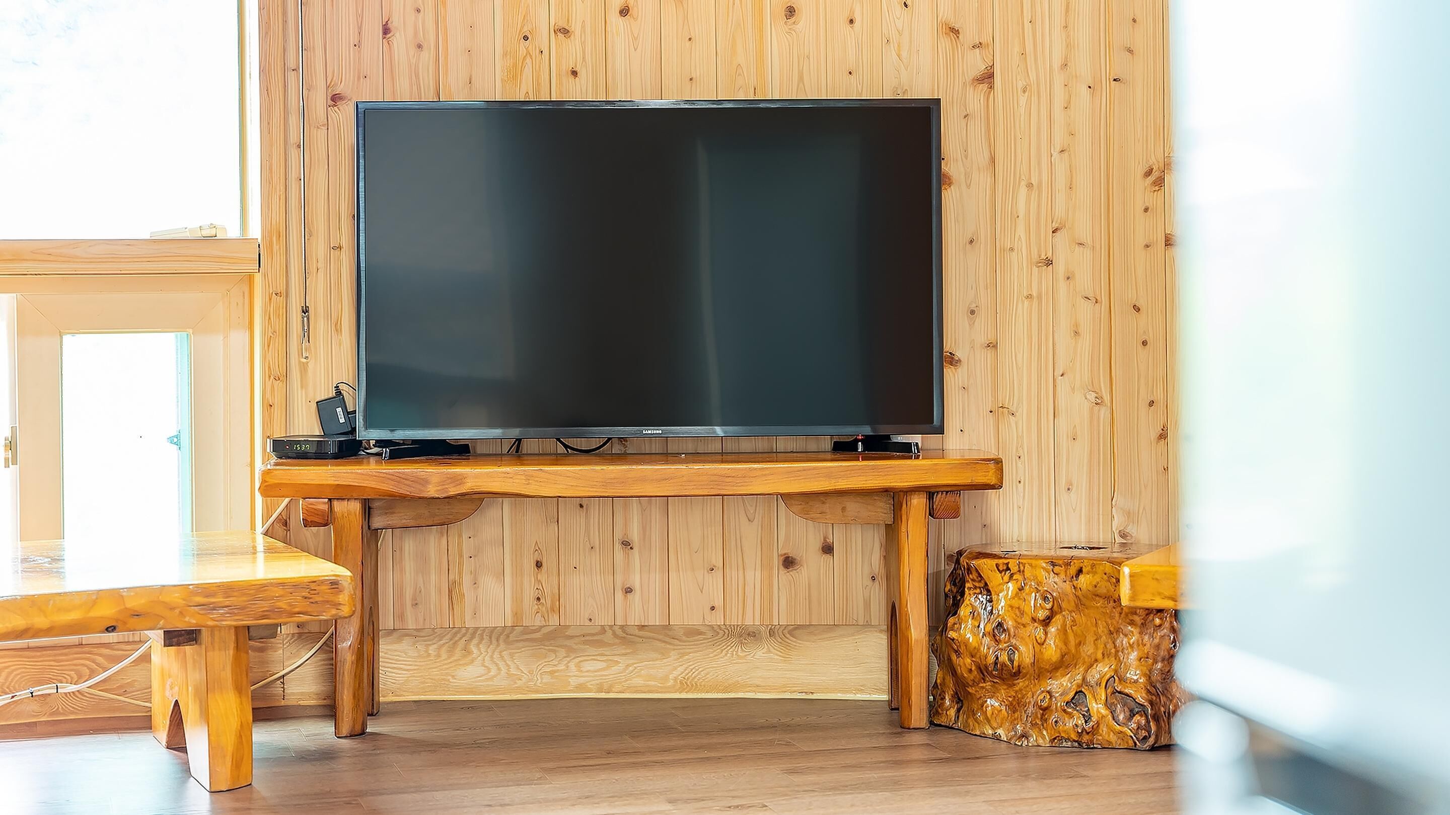 Un salon moderne doté d’un grand téléviseur à écran plat fixé à un mur en bois, d’une table à manger en bois et d’une sculpture en bois originale.