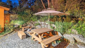 Un patio al aire libre con mesas y bancos de madera, rodeado de rocas y follaje.
