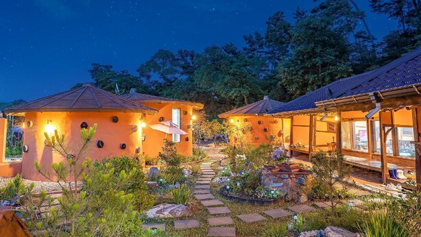 Zona exterior acollidora i ben il·luminada amb dues construccions petites, un camí de pedra i vegetació abundant.