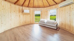 Habitació de fusta amb sostre inclinat, un llit amb llençols ben arrufades i una finestra que mostra un paisatge verd.