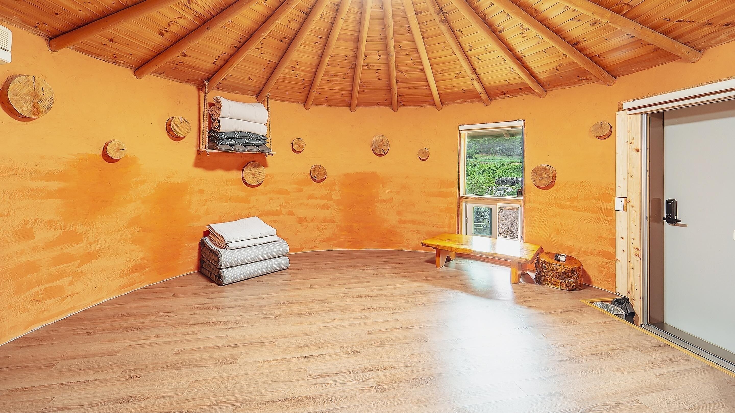 Une pièce avec un plafond en bois, un banc, une porte et une fenêtre donnant sur un paysage verdoyant.