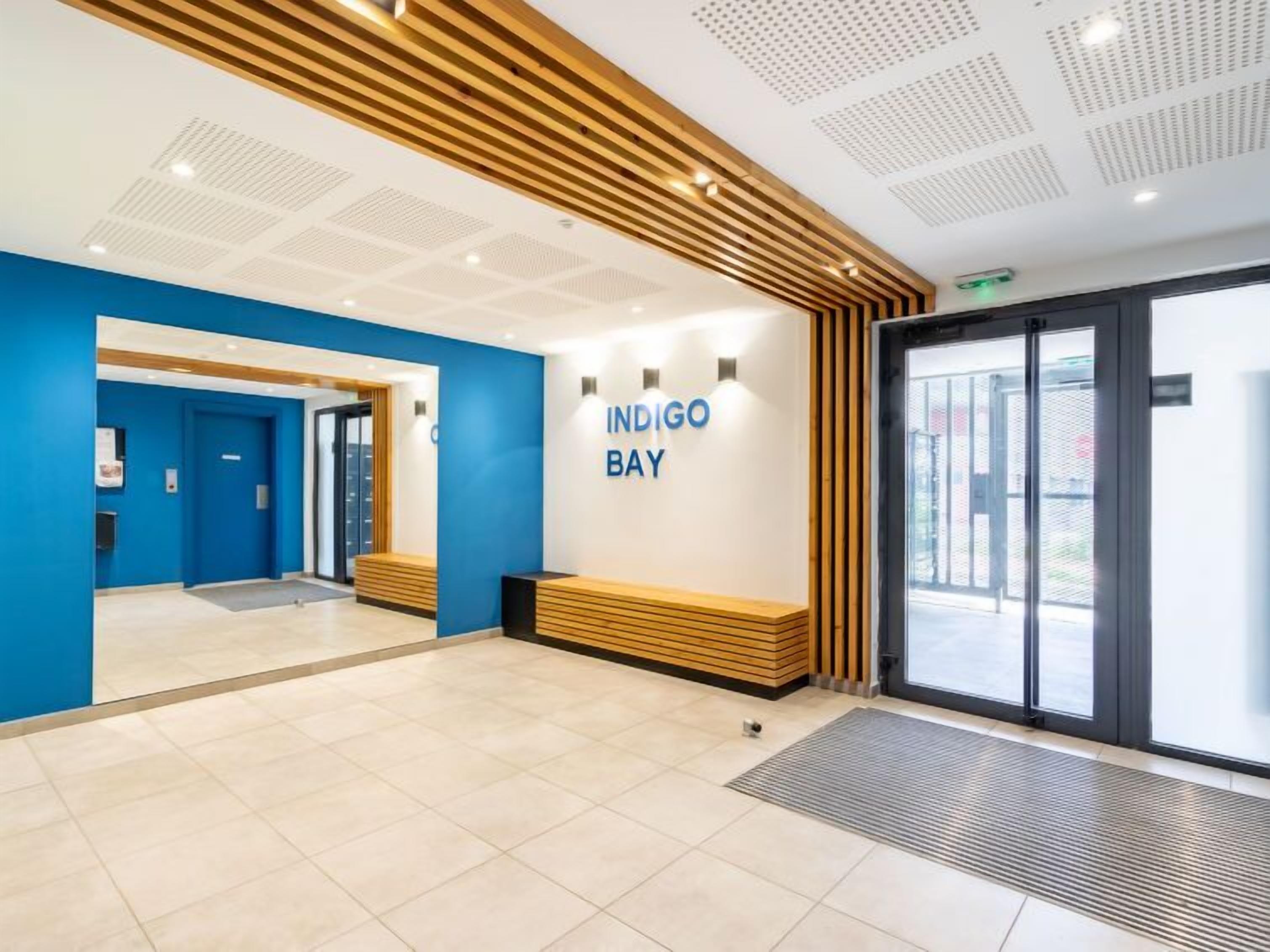 Un espace d’accueil moderne avec un mur bleu, un banc en bois et une porte en verre.