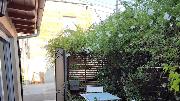 Une terrasse en bois mène à un petit espace de détente extérieur, agrémenté d’une table et de chaises, et entouré de verdure et d’une clôture en bois.