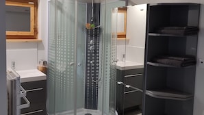 Une salle de bain moderne dotée d’une douche à parois de verre, d’un meuble-lavabo avec miroir et d’étagères intégrées.