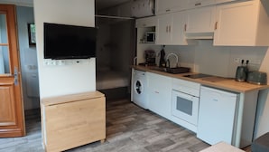 Une cuisine compacte équipée d’un lave-linge, d’un four à micro-ondes et d’un petit meuble en bois.