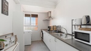A modern kitchen with white cabinetry, a stainless steel range hood, a built-in microwave, and a window with blinds. - Casa Angel Malaga (Málaga)