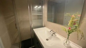 A bathroom with a glass shower enclosure, a white sink, and a mirror with a floral arrangement. - Casa Angel Malaga (Málaga)