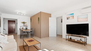 A modern living room with a sofa, a coffee table, a TV, a dining area with chairs, and a kitchen area. - Casa Angel Malaga (Málaga)