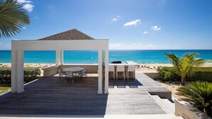 Un patio in legno con un gazebo, un tavolo e sedie con vista sulla spiaggia.