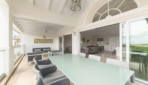Una habitación amplia con una gran mesa de comedor, sillas grises tapizadas, un sofá y un ventanal con vistas al exterior.