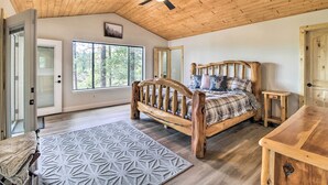 Ein Deckenventilator aus Holz, ein Bett mit kariertem Überwurf, ein Nachttisch aus Holz und ein gemusterter Teppich.