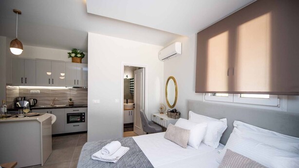 Quarto de hotel moderno com uma cama grande, uma pequena cozinha, um banheiro e vista para o exterior.