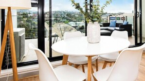 A modern room with a round table, white chairs, a vase with green plants, and a view of the city through large windows. - Aqua Views of the bay in Mornington (Mornington)