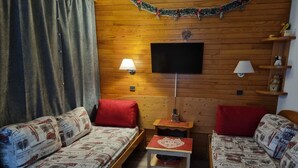Una habitación acogedora con dos sofás de madera, una mesita pequeña de madera, un televisor en la pared y una guirnalda navideña.