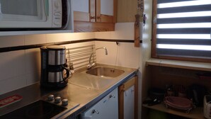 Una cocina compacta con microondas, cafetera, lavamanos y armarios de madera.