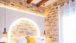 Un dormitorio con pared de piedra, cama con ropa de cama blanca y amarilla, y vigas de madera en el techo.