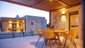 Un patio al aire libre con un edificio de piedra, una pérgola de madera y sillas de mimbre.