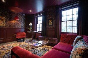 A room with a red sofa, a red armchair, a patterned rug, a small table with a tray, and a window with curtains. - Sun Street Hotel Shoreditch (London)