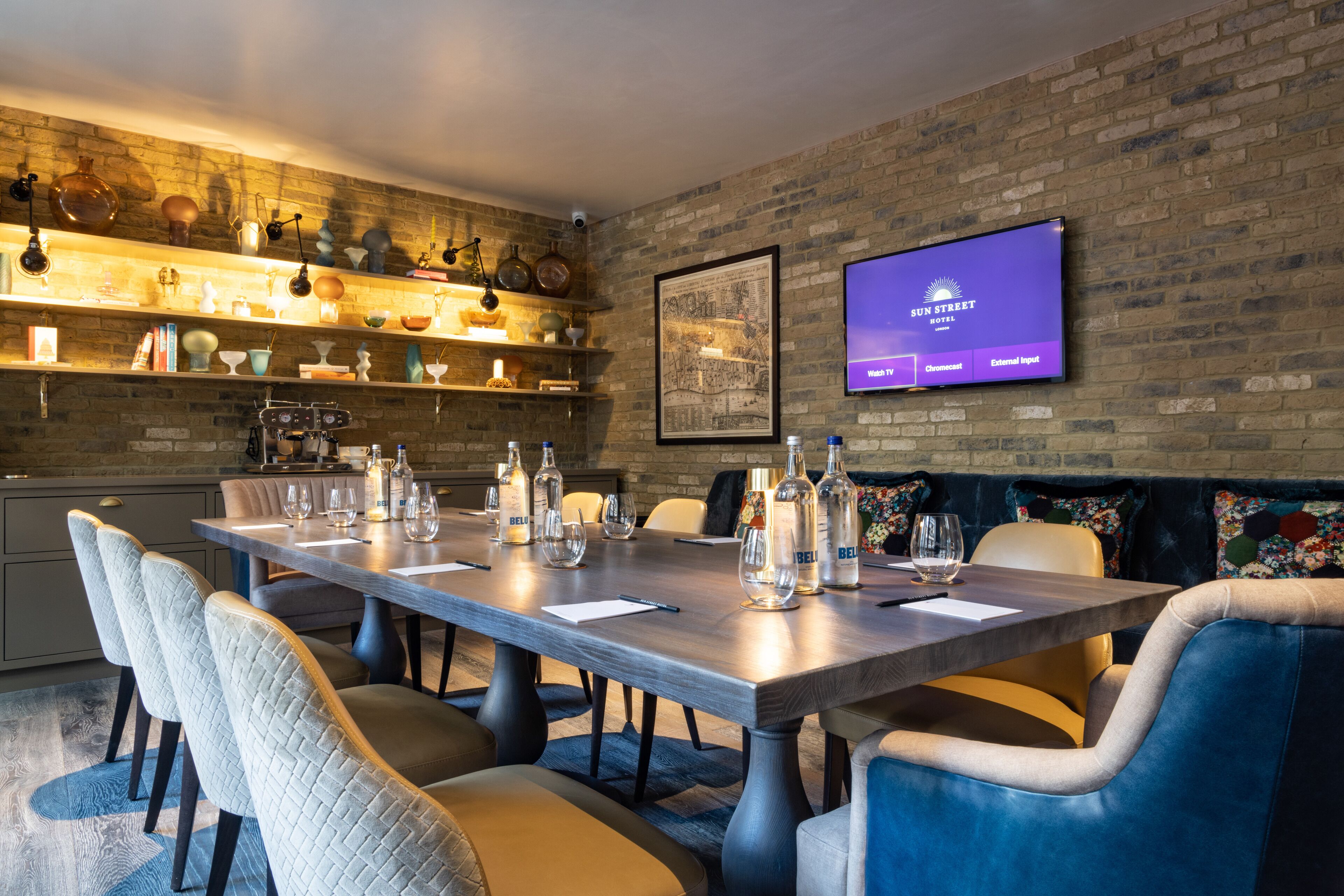 A modern dining area with a long table, comfortable seating, and a television displaying 'Sun Street Hotel'.