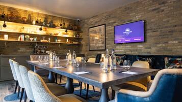 A modern dining area with a long table, comfortable seating, and a television displaying 'Sun Street Hotel'.