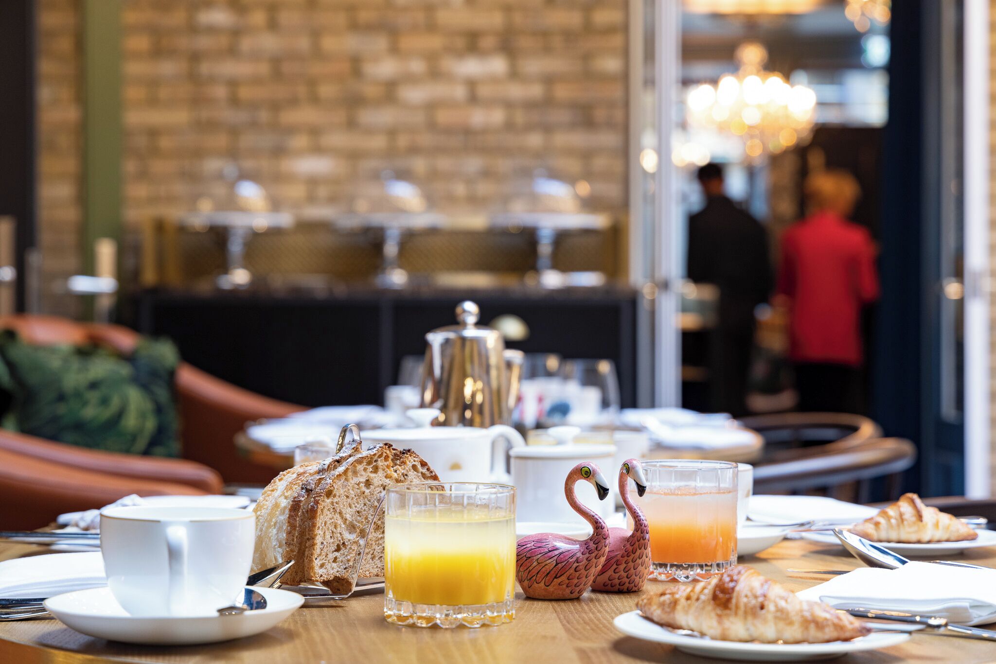 Ein Frühstückstisch mit Croissants, Orangensaft und einem glasklar gläsernen Flamingo.