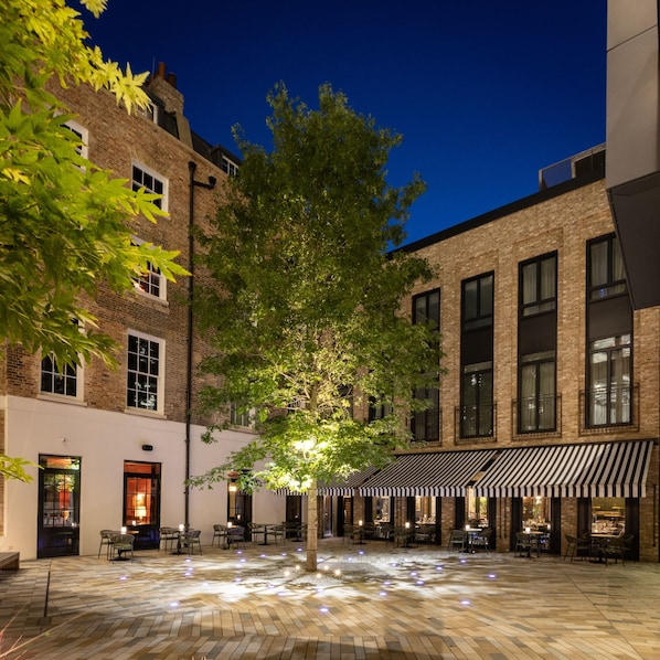 An outdoor cafe area with brick buildings, tables, and chairs. - Sun Street Hotel Shoreditch (London)