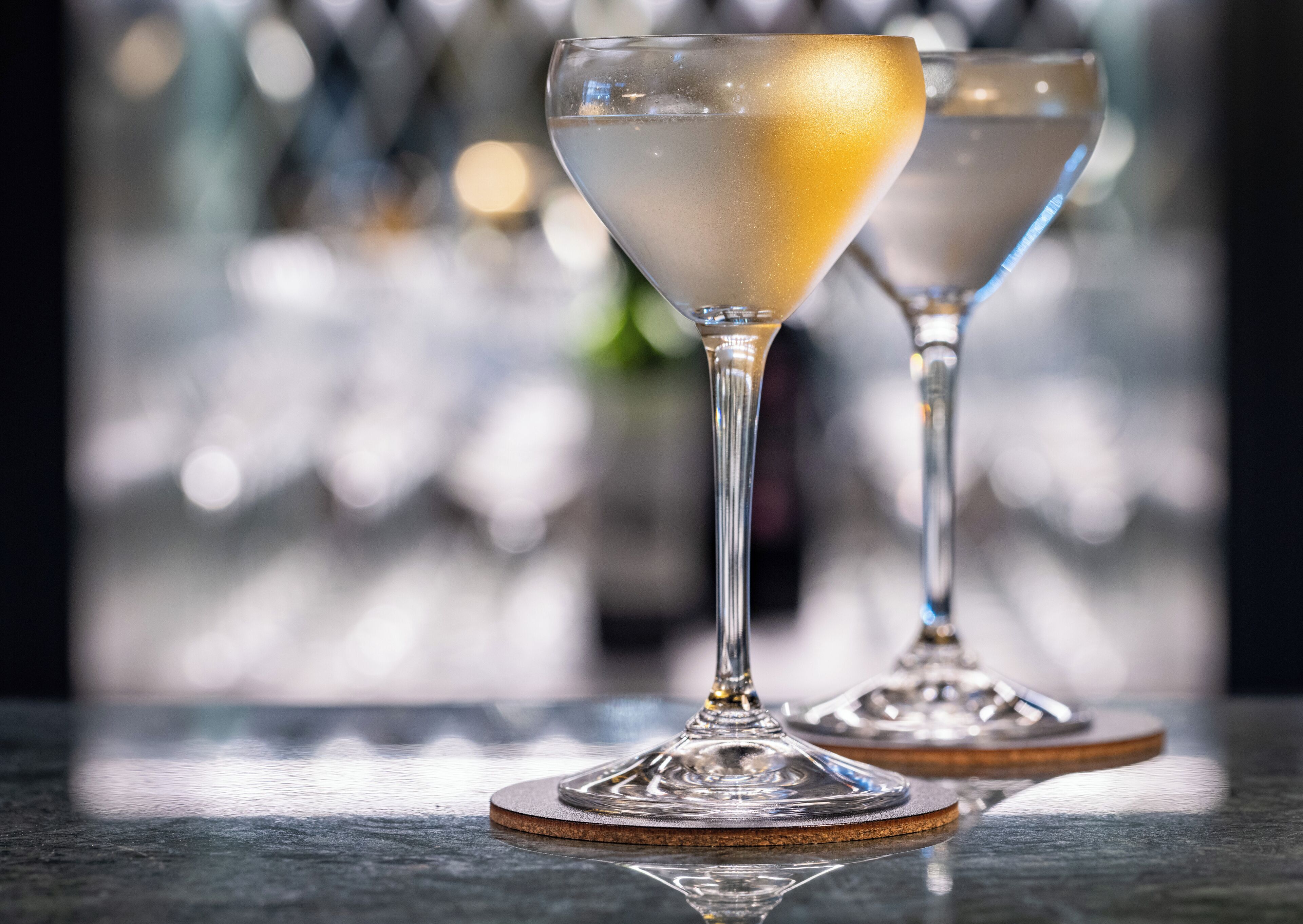 Two glasses of a clear beverage with a golden rim on a reflective surface.